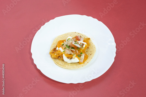 Solitary chicken tinga taco with white onion, unrecognizable sauce and wheat tortilla on white plate