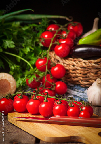 bunch of fresh cherry tomatoes with green stems on a kitchen board and raw spices, selective focus