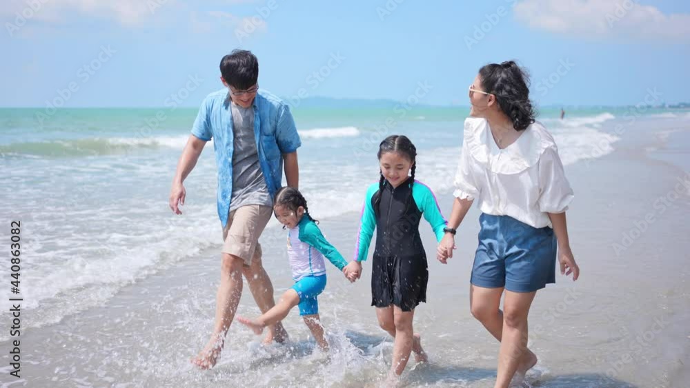 Asian family on summer vacation. Parents with two child girl kid walking on the beach with playing sea water together. Two sisters sibling having fun outdoor lifestyle activity with father and mother.