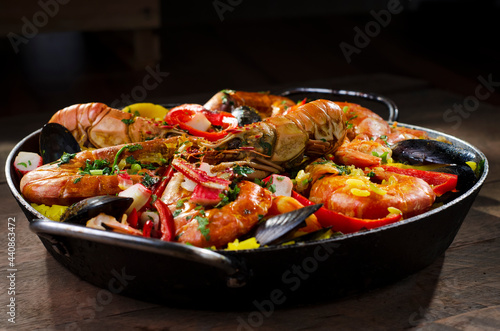 Paella traditional Spanish dish, served in the paella pan on a rustic wooden table highlighting the ingredients, shrimp, lobster, mussels, rice, red pepper and spices