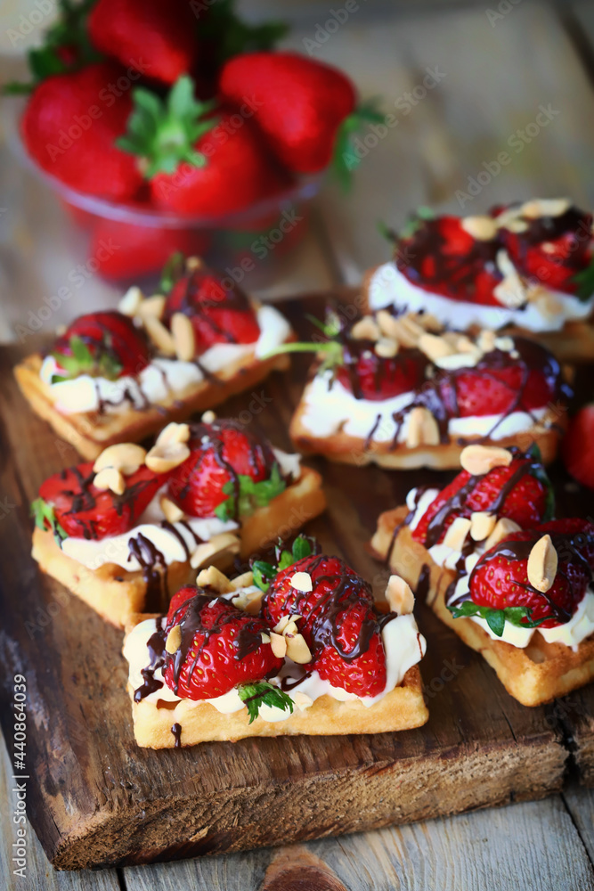 Waffles with fresh strawberries, cream cheese and chocolate on a wooden board. Healthy summer dessert.