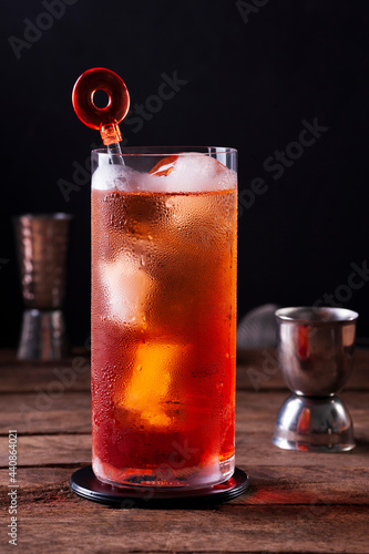 a glass with aperol and tonic on a rustic wooden table with bar utensils unfocused in the background, black background, copy space