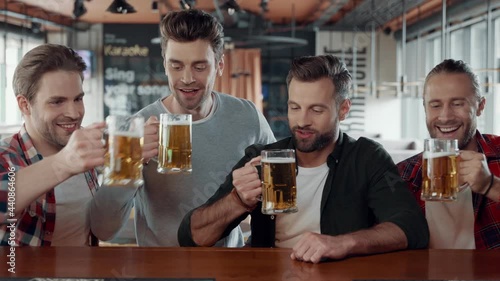 Happy young men in casual clothing toasting each other with beer the pub
