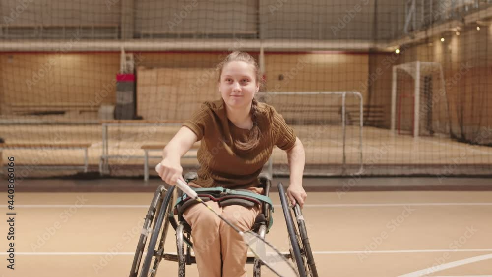 Blond-haired Caucasian handicapped sportsgirl in wheelchair playing badminton, hitting shuttle with racket in gymnasium Blond-haired Caucasian handicapped sportsgirl in wheelchair playing badminton, hitting shuttle with racket in gymnasium