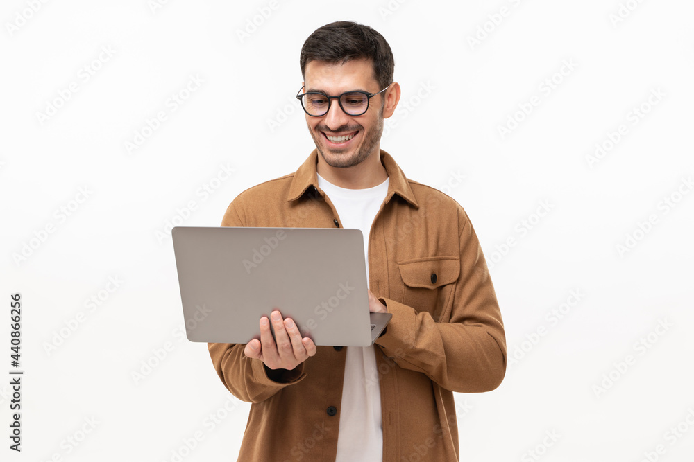 Young happy man standing with opened laptop, browsing online or typing message, isolated on gray background Young happy man standing with opened laptop, browsing online or typing message, isolated on gray background