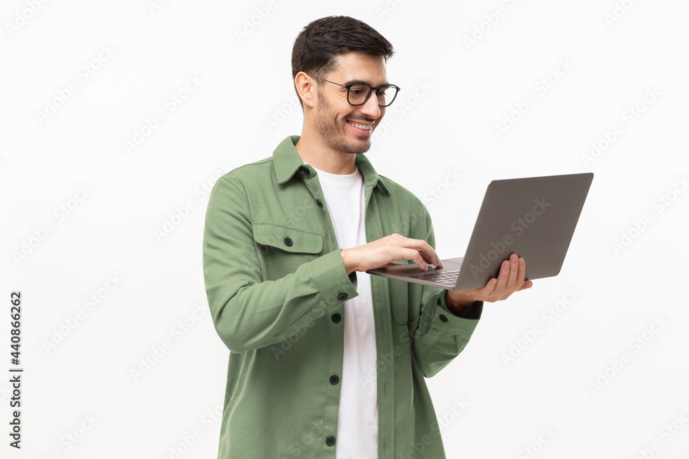 Young man wearing casual green shirt, standing with opened laptop in hands, surfing online, isolated on gray background Young man wearing casual green shirt, standing with opened laptop in hands, surfing online, isolated on gray background