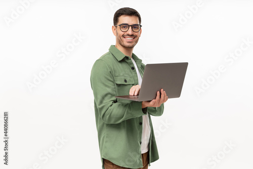 Portrait of young modern businessman standing holding laptop and looking at camera with happy smile, isolated on gray photo