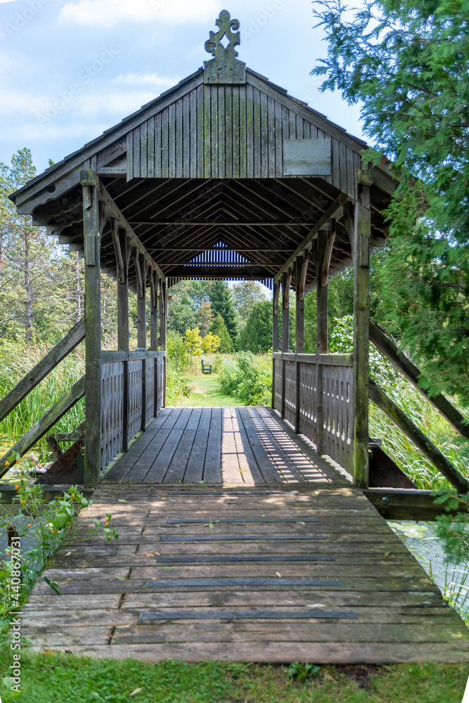 A small, covered footbridge crosses a stream and leads into a peaceful, tranquil, lush nature preserve in Ontario.