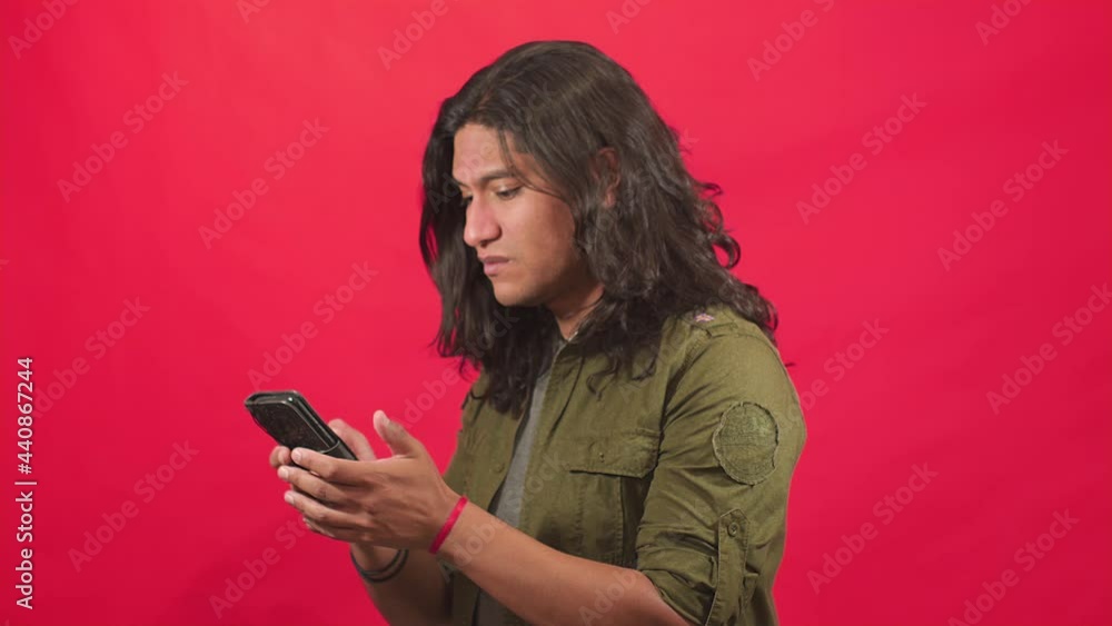 Man checks his smartphone, gets angry when he sees your messages, he makes an angry face and crosses his arms in disapproval, Video in a studio with a red background Man checks his smartphone, gets angry when he sees your messages, he makes an angry face and crosses his arms in disapproval, Video in a studio with a red background