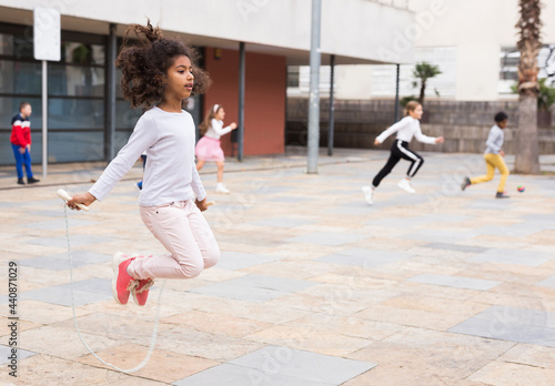 Obraz na plátně Cute tween African American girl skipping rope in schoolyard during break betwee
