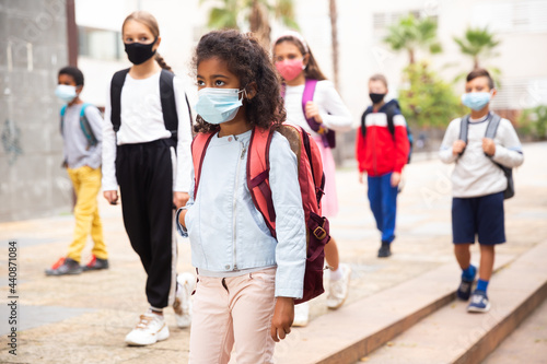 Portrait of tween girl in medical face mask on her way to college on warm autumn day. Forced precautions in COVID pandemic