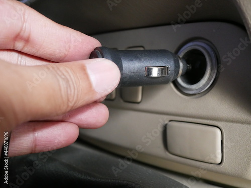 hand holding plug 12 volt into socket from car cigarette lighter. 