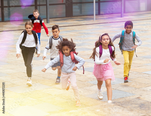 Team of positive schoolchildren running in race in the street and laughing outdoors