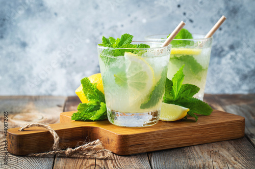 Two glass with lemonade or mojito cocktail with lemon and mint, cold refreshing drink or beverage with ice on rustic blue background. Copy space
