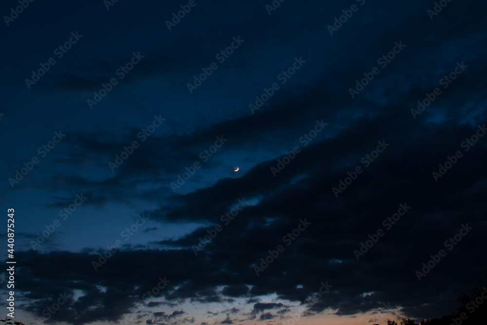 Silhouette picture of dark cloudy blue sky and waxing crescent moon in middle