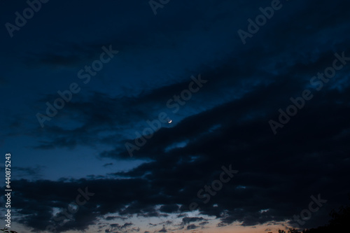 Silhouette picture of dark cloudy blue sky and waxing crescent moon in middle