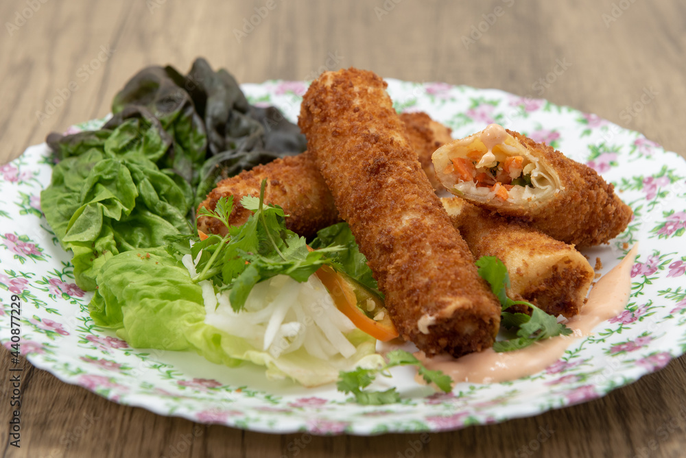 Hearty appetizer of breaded, deep fried egg rolls full of vermicelli and vegetables served on a flowered plate