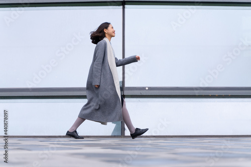 full length side view of Young stylish Chinese businesswoman walking outside modern office building glass window in the Chengdu City