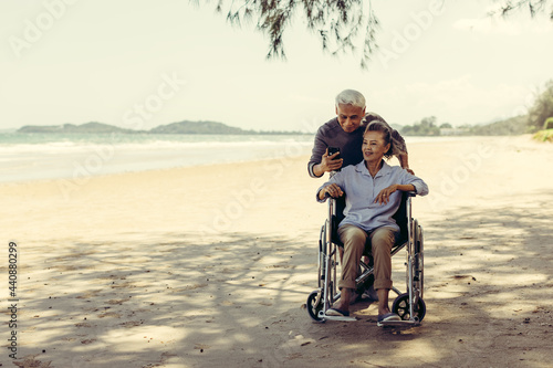 retired couple Husband pushes a wheelchair to his wife The couple was happy at the sandy beach. Retirement couple concept and health care.