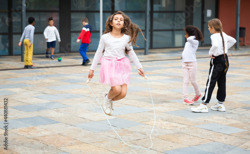 Happy schoolgirl jumping game by rubber band, kids friends on background © JackF