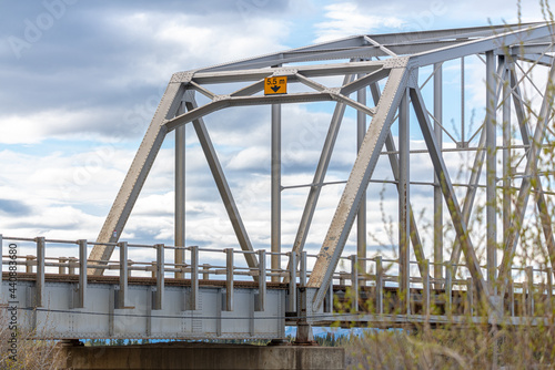 Large man made structure steel bridge spanning across Nisutlin Bay in township of Teslin flowing to the Yukon River in northern Canada during spring summer time with cloudy blue sky background. photo