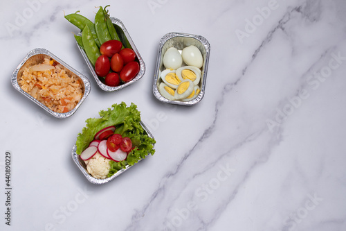 Take away healthy food in foil boxes on marble table. Copy space