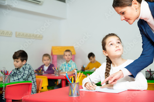 Female teacher helps schoolgirl complete an assignment in an elementary school class