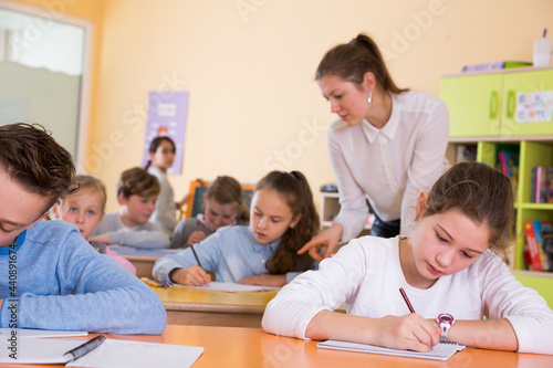 Group of school kids with pens and notebooks studying in classroom with teacher © JackF