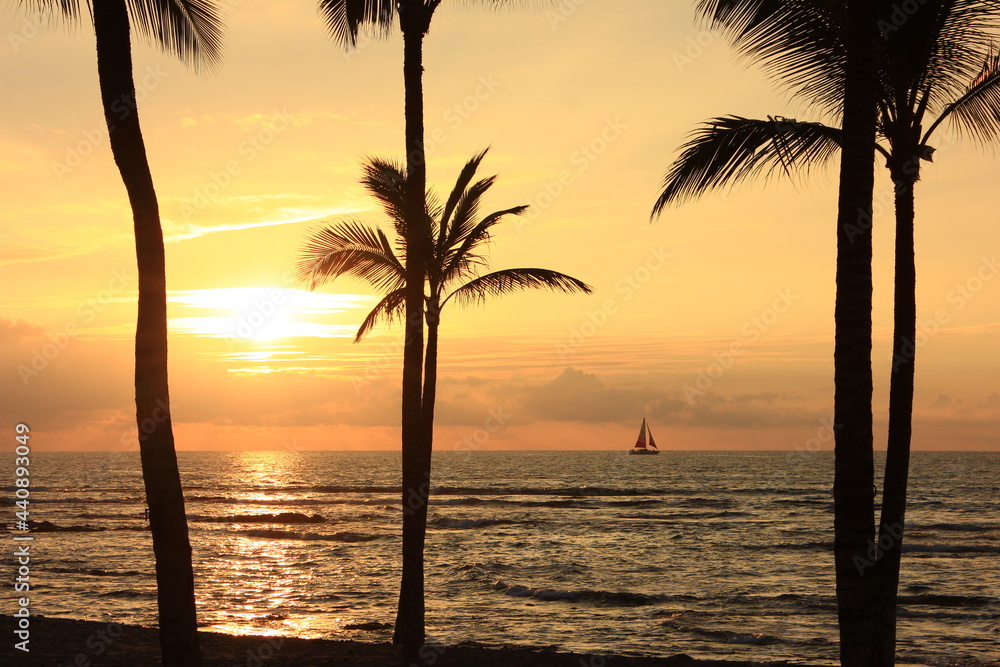 ハワイ島(ビッグアイランド）。一艘のヨットが浮かぶ海に沈む夕日。	
