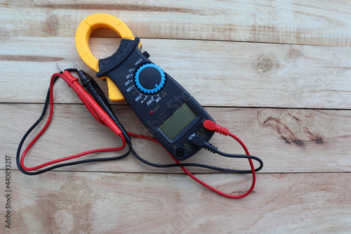 Digital clamp-on meter with probes, electrical measuring instruments isolated on wooden background closeup.