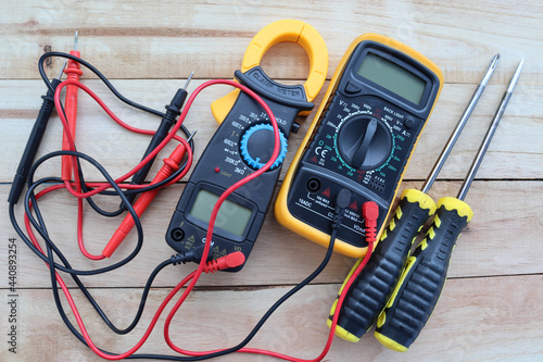 Digital multimeter, clamp-on meter with probes, electrical measuring instruments, and screwdrivers isolated on wooden background closeup.