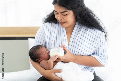 Mother carrying and feeding newborn baby with milk bottle. Newborn born or infant eating milk from nipples while mom holding milk bottle