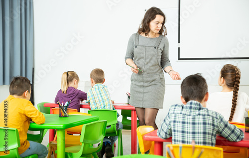 Young female teacher standing at whiteboard in classroom, conducting lesson with children