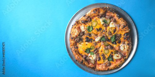 Whole cheese and meat pizza over blue background. Pizza with onions and pickles served on a metal tray.