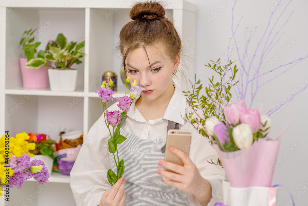 The girl florist takes pictures on the phone of a flower arrangement standing on a wooden background. Opening of the flower business The girl florist takes pictures on the phone of a flower arrangement standing on a wooden background. Opening of the flower business