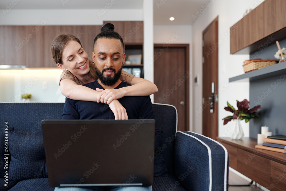 Happy young woman hugging her husband from behind when he is coding on ...