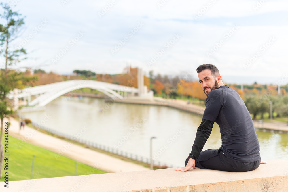 Sportsman with headphones sitting facing the camera in a park