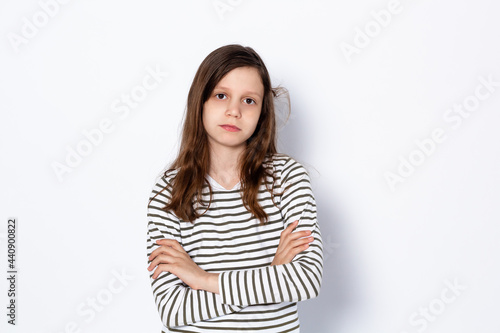 A sad dark-haired teenage girl stands with her arms crossed. On a light background. Portrait. Place for your text. © Евгения Надежина