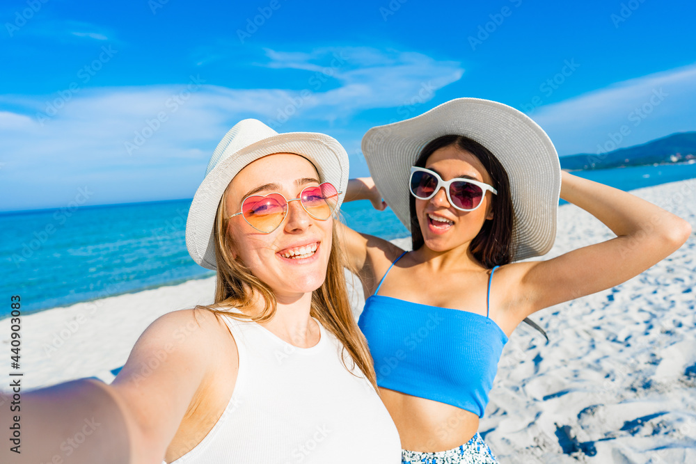 Two girls taking a self-portrait with cell wearing blue casual summer clothes and funny sunglasses on vacation at tropical beach resort. Beauty young women couple enjoying travel using smartphone Two girls taking a self-portrait with cell wearing blue casual summer clothes and funny sunglasses on vacation at tropical beach resort. Beauty young women couple enjoying travel using smartphone