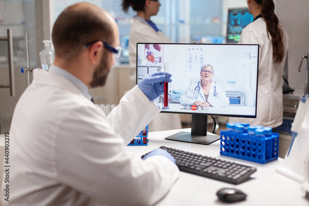 Reseacher holding blood sample discussing treatment with doctor during virtual video call. Scientist examining vaccine evolution using high tech researching treatment, health innovation, staff