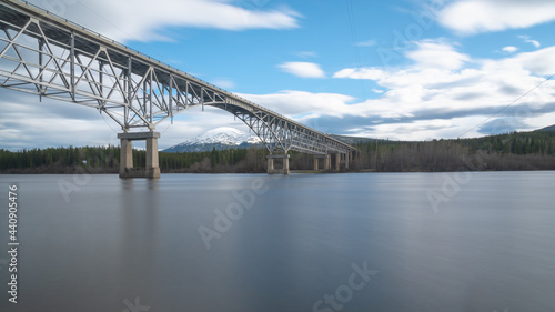Johnsons Crossing, Teslin River steel Bridge on the Alaska Highway with long exposure shot of calm, silky looking water and cloudy, blue sky sunset afternoon. 