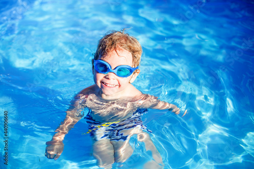 Beautiful toddler child, blond boy, swimming in a pool in backyard