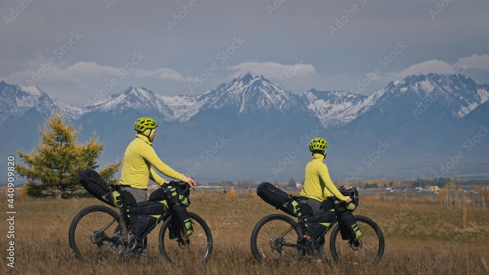 The man and woman travel on mixed terrain cycle touring with bikepacking. The love couple journey with tent in nature with bicycle bags. Stylish bikepacking, bike, sportswear in green black colors.