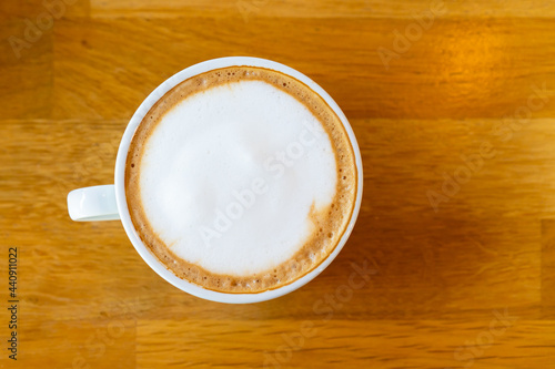 Beautiful surface of hot latte coffee in a cup from top view served on the wooden table. Photograph of latte coffee from top view on wooden table close up.