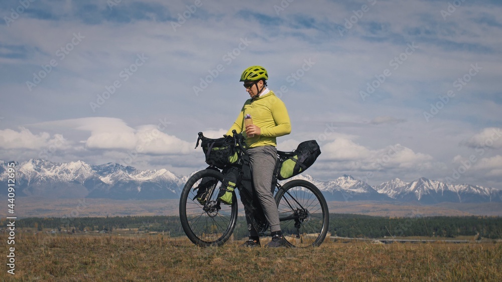The man travel on mixed terrain cycle touring with bikepacking. The traveler journey with bicycle bags. Sport bikepacking, bike, sportswear in green black colors. Mountain snow capped, stone arch. The man travel on mixed terrain cycle touring with bikepacking. The traveler journey with bicycle bags. Sport bikepacking, bike, sportswear in green black colors. Mountain snow capped, stone arch.