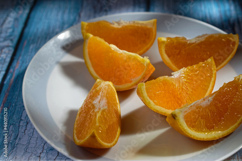 Close-up of an orange cut into wedges  on a plate on a blue table.