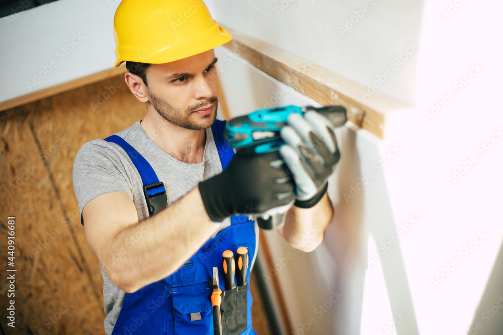 Young home repair male or worker busy with house renovation, holds building equipment, wears casual working clothes in the new build Young home repair male or worker busy with house renovation, holds building equipment, wears casual working clothes in the new build