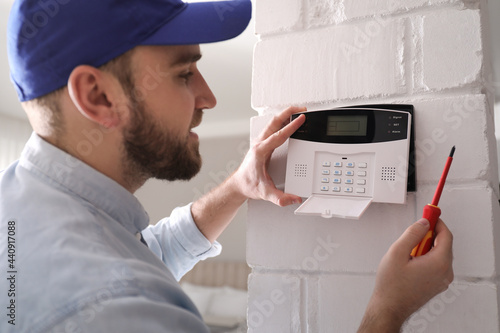 Man installing home security system on white wall in room