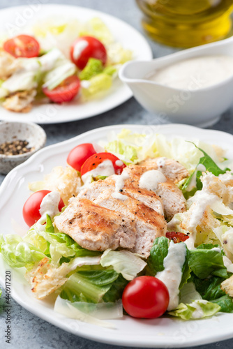 Caesar salad with grilled chicken breast and sauce on a plate, closeup view