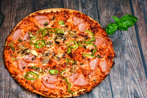  Close up of classic italian pizza with ham. Fresh basil,tomato sauce ,mozzarella cheese , mushrooms and green peppers